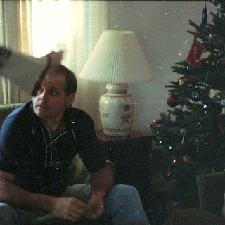 Man sitting indoors near Christmas tree.