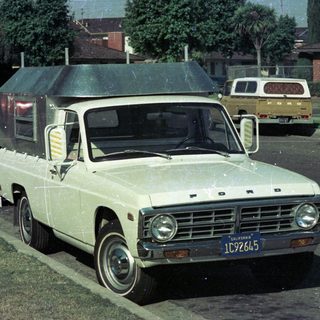 Vintage white Ford pickup truck with camper shell parked.