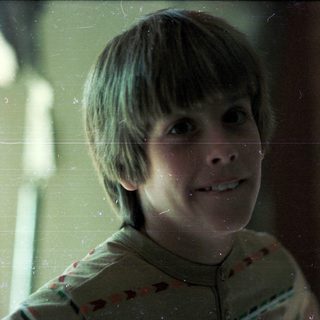 Young boy smiling through rain-streaked window.
