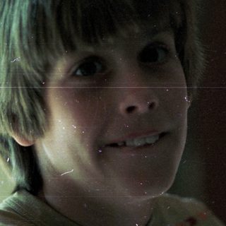Young boy smiling through rain-streaked window.