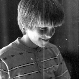 A smiling child playing with water droplets on a window.