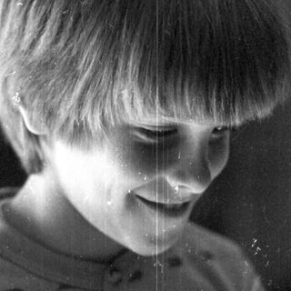 A smiling child playing with water droplets on a window.