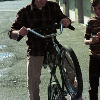 Two boys walking with bicycles outdoors.
