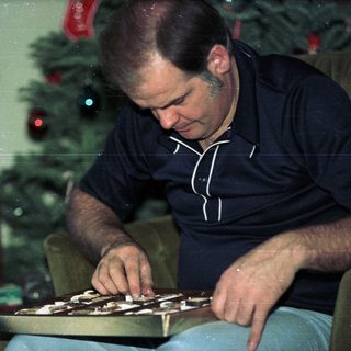 Man wrapping a striped gift box near a Christmas tree.