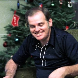 Smiling man in dark shirt near decorated Christmas tree.