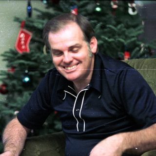 Smiling man in dark shirt near decorated Christmas tree.