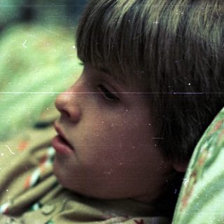 Boy resting with head on camouflage jacket.