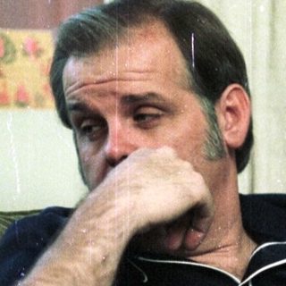 Man sitting thoughtfully indoors, resting chin on hand.