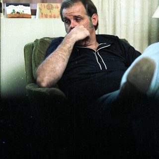 Man sitting thoughtfully indoors, resting chin on hand.