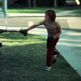 Two children playing baseball in a driveway.