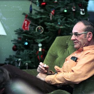 Man sitting in armchair by decorated Christmas tree.