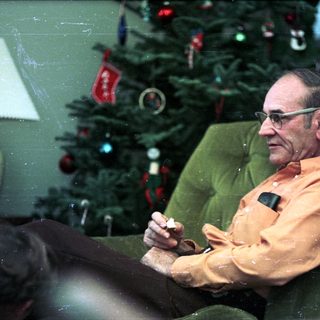 Man sitting in armchair by decorated Christmas tree.