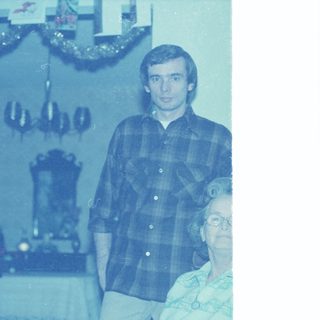 Young man in plaid shirt with elderly woman indoors.