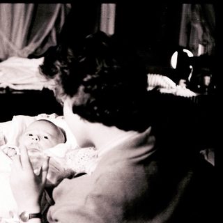 A woman cradles a newborn baby indoors.