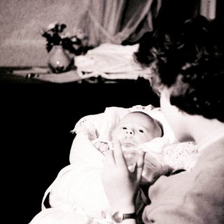 A woman cradles a newborn baby indoors.
