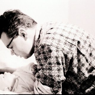 A man gently holds and examines a newborn baby.