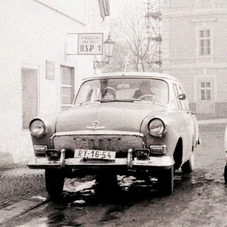 Old-fashioned car parked with man pushing laundry cart.