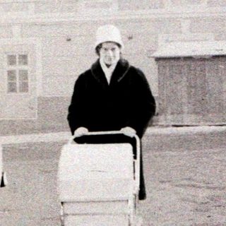Old-fashioned car parked with man pushing laundry cart.