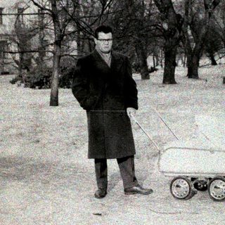 Man pushing small wheeled cart in snowy park.