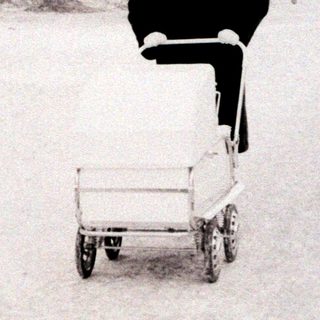 Person pushing wheelbarrow through snowy park.