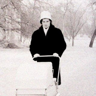 Person pushing wheelbarrow through snowy park.
