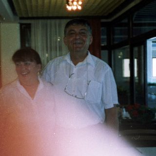 Two people smiling indoors near kitchen area.