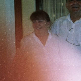 Two people smiling indoors near kitchen area.