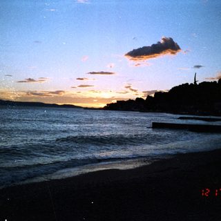 Sunset over calm ocean shoreline with clouds.