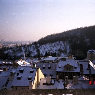 Snow-covered cityscape with rooftops and hills.