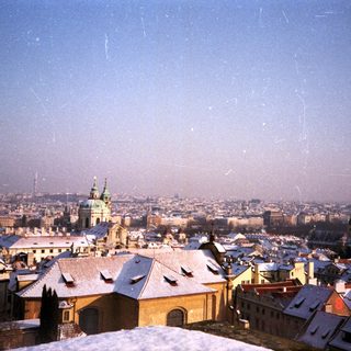 Snow-covered historic cityscape with rooftops and church spires.
