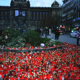 Memorial with numerous candles and flowers in city square.