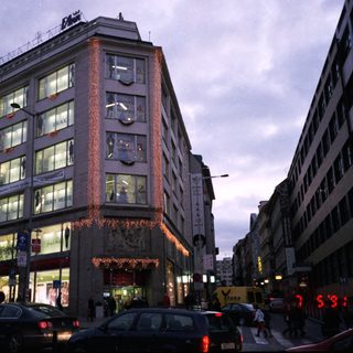 Urban street scene with illuminated storefronts and evening traffic.