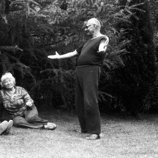 Three people outdoors, man gesturing, seated elderly and child.