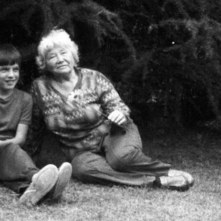 Three people outdoors, man gesturing, seated elderly and child.