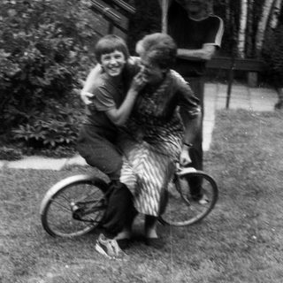 Two children joyfully hugging on a bicycle.