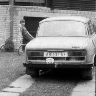 Vintage car parked outside wooden house with open gate.