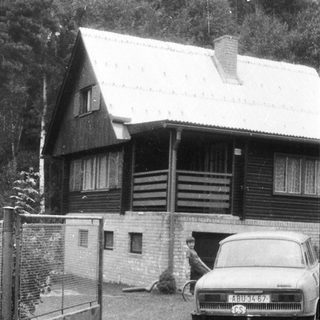 Vintage car parked outside wooden house with open gate.