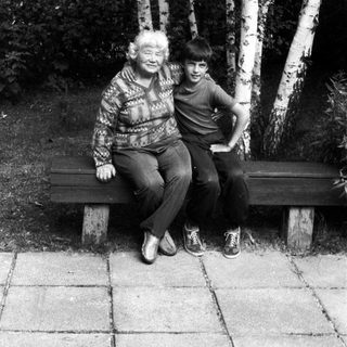 Two people sitting closely on a bench outdoors among birch trees.