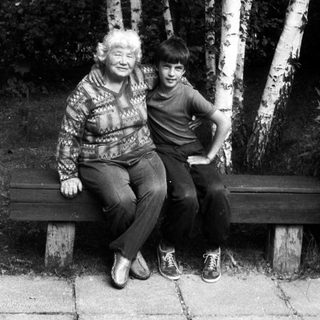 Two people sitting closely on a bench outdoors among birch trees.