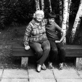 Two people sitting closely on a bench outdoors among birch trees.