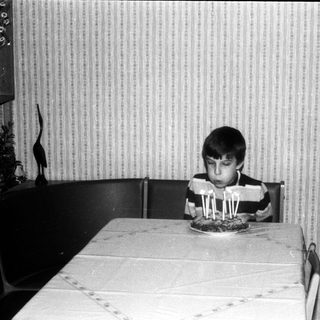 Young boy sitting at table blowing out birthday candles.