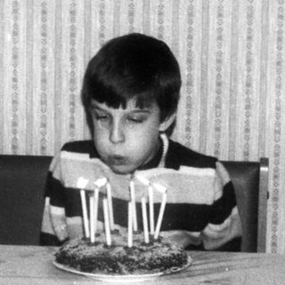Young boy sitting at table blowing out birthday candles.