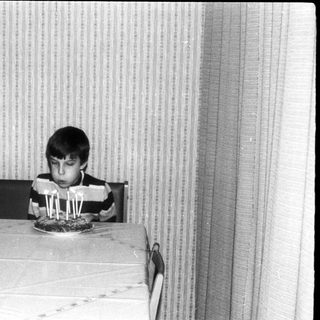 Young boy sitting at table blowing out birthday candles.