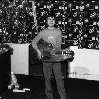 Young boy playing acoustic guitar indoors during holiday season.