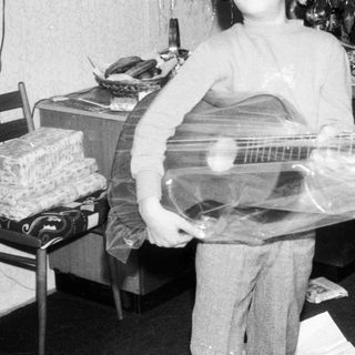 Young boy holding wrapped electric guitar indoors.