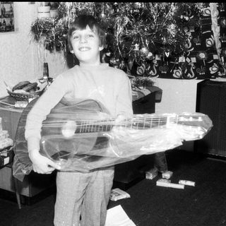Young boy holding wrapped electric guitar indoors.