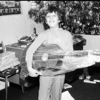 Young boy holding wrapped electric guitar indoors.
