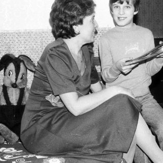 Two people reading together indoors, likely in a living room.