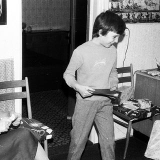 Family scene: Woman sewing, boy playing with toy.
