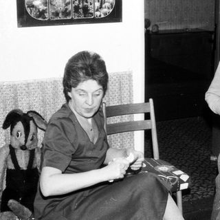 Family scene: Woman sewing, boy playing with toy.
